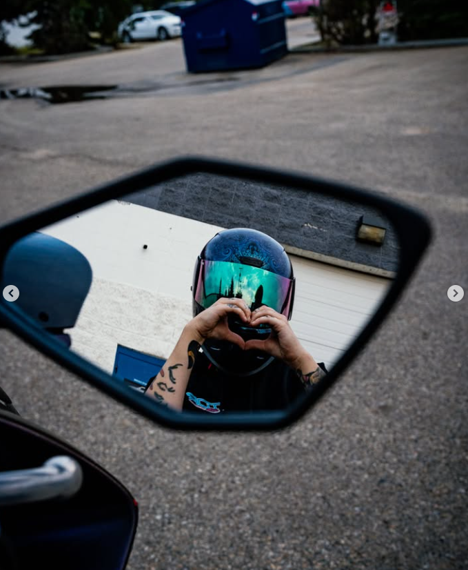 Kay reflected in a vehicle mirror while wearing a motorcycle helmet