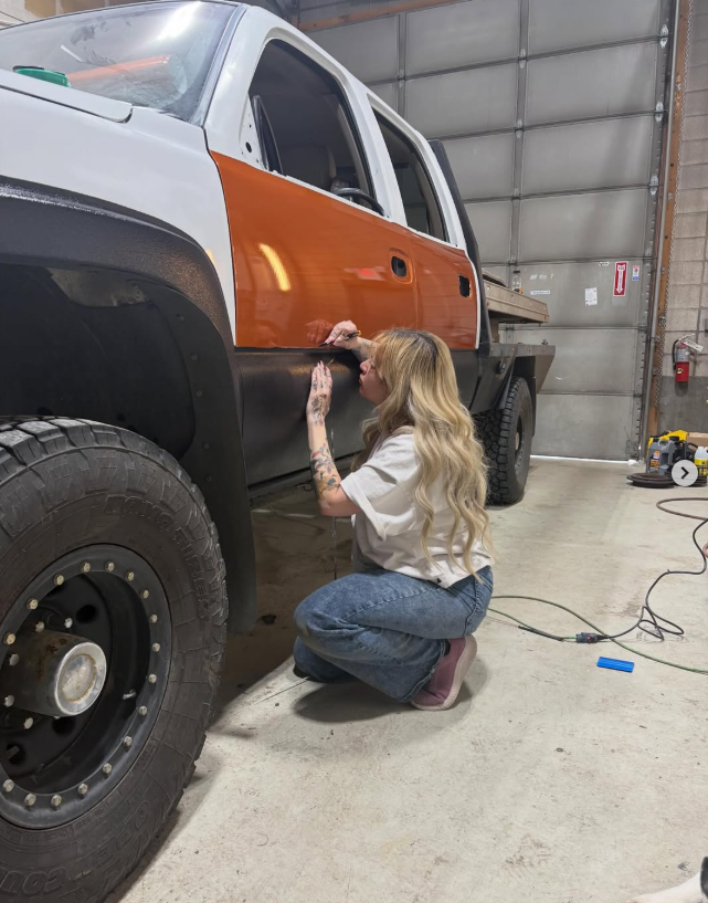Kay working carefully along the side panel of a two-tone truck