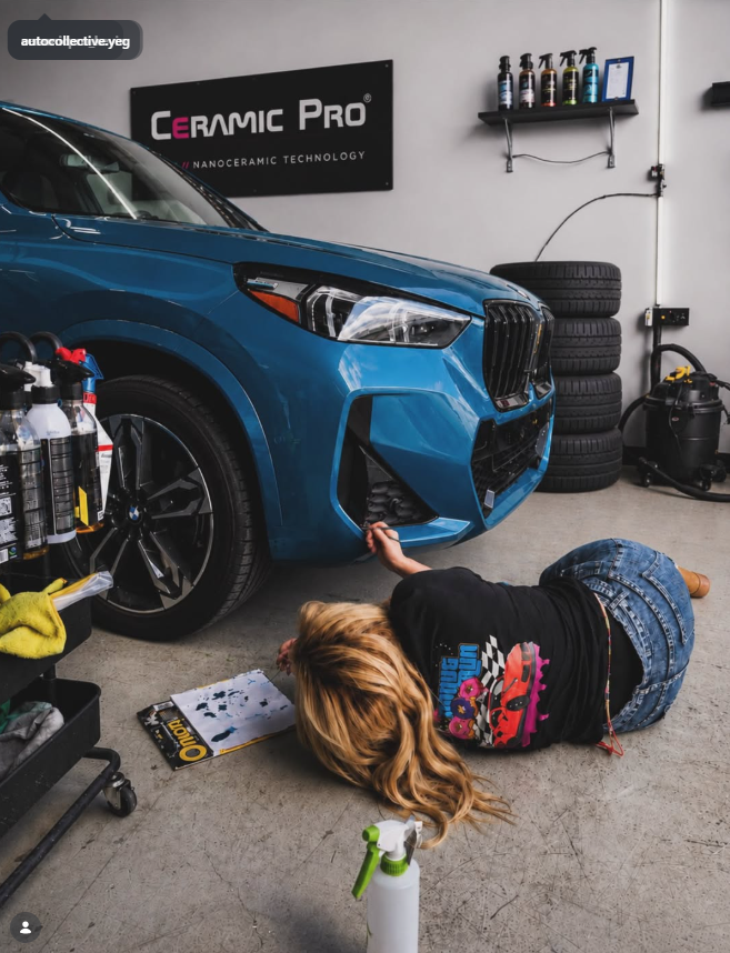 Kay working beside a blue BMW at The Auto Collective shop